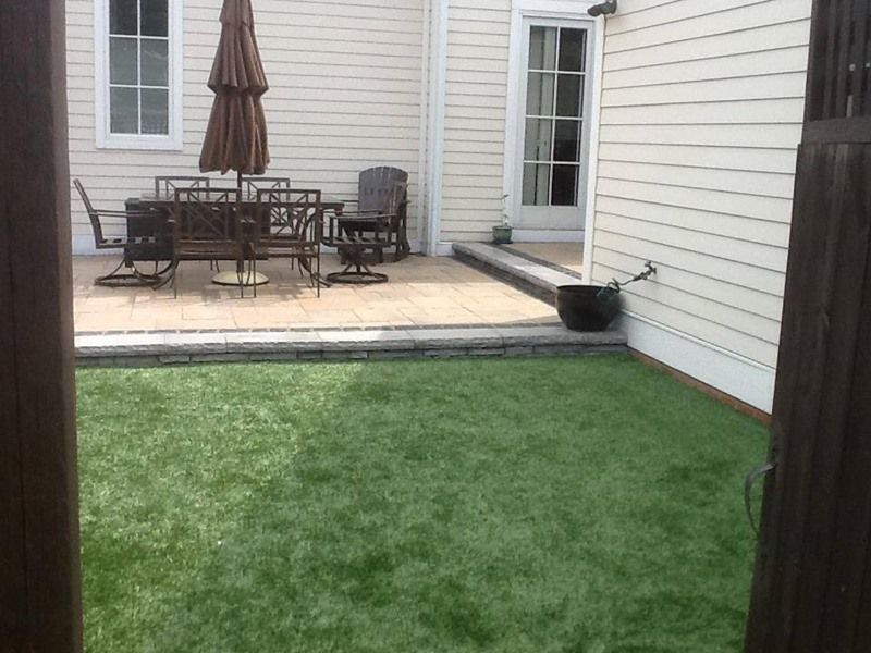 Patio with brown furniture, umbrella, and grass, viewed from a wooden gate.