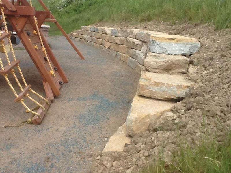 Stone retaining wall with steps next to playground equipment and grassy hill.