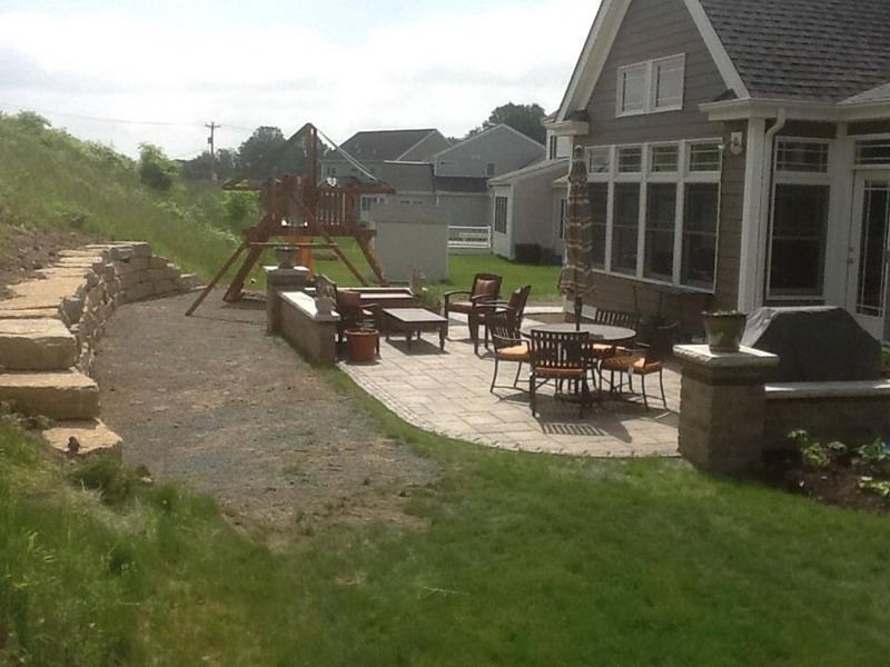 Patio with outdoor furniture, next to a house and a play set on a grassy hill.