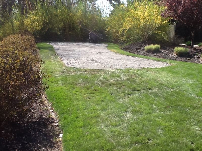 Gravel parking area in a yard, surrounded by green grass and shrubs with yellow and brown foliage.