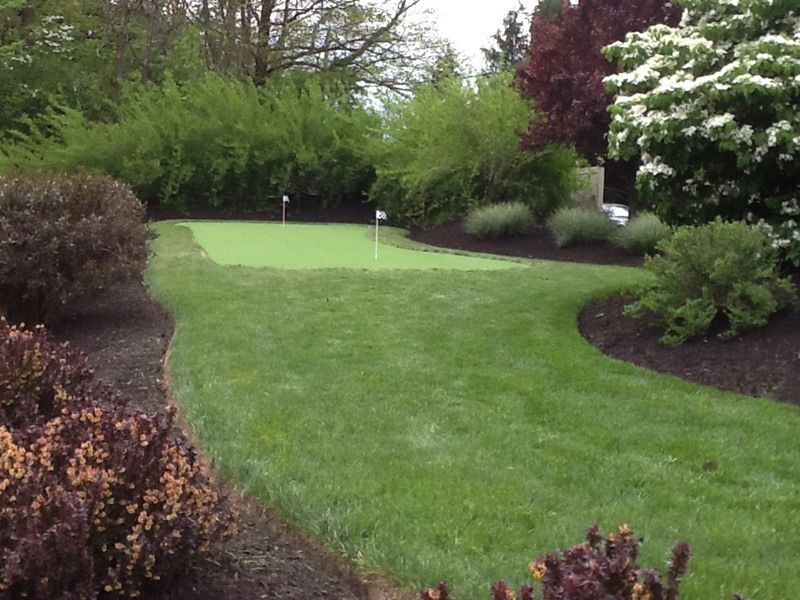 A backyard putting green with a fairway surrounded by landscaping.