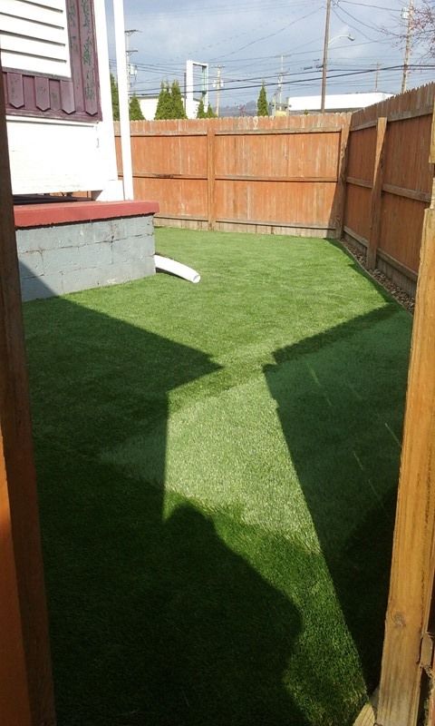 Small backyard with artificial turf, wooden fence, and white house exterior.