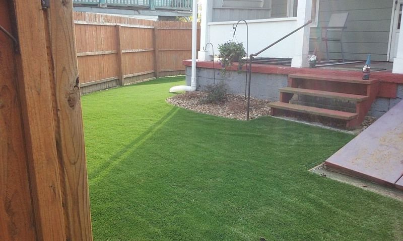 Green lawn enclosed by a wooden fence and a house with steps and a porch.
