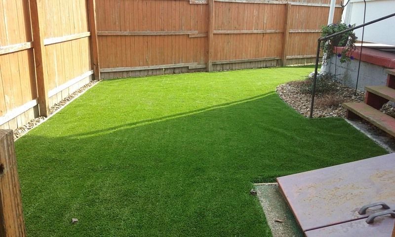 Artificial turf backyard with wooden fence and steps.
