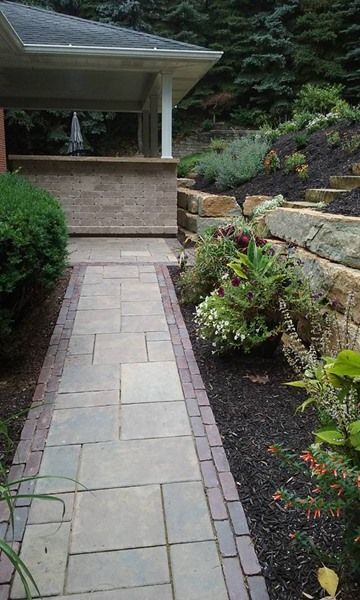 Stone pathway leading towards a patio with a raised garden bed and retaining wall.
