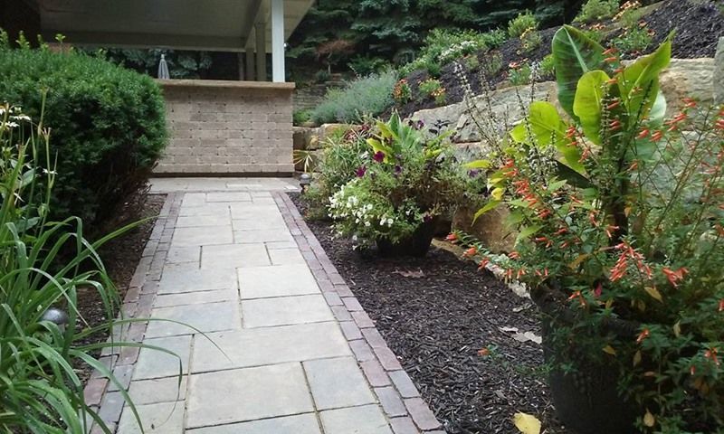 Stone walkway lined with colorful flowers and shrubbery leading to a porch.
