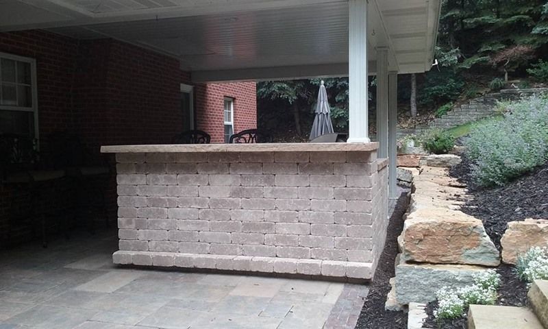 Brick bar under a covered patio. Outdoor setting with a stone border and hillside.