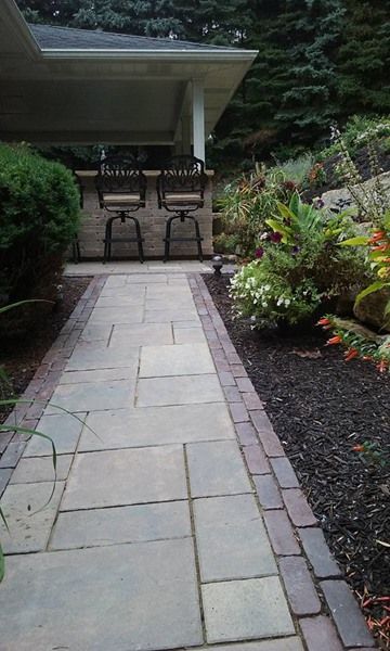 Stone path leading to an outdoor bar with stools, surrounded by flowerbeds.
