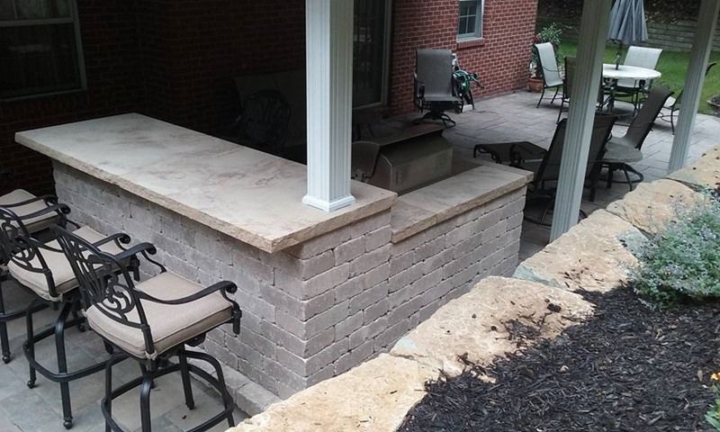 Outdoor kitchen with brick facade, concrete countertop, built-in grill, and bar seating.