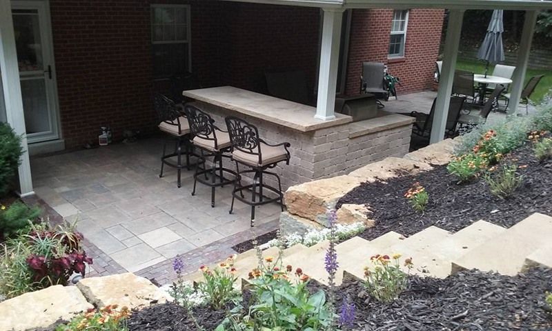 Outdoor patio with a brick bar, stools, and stone steps leading to a garden.