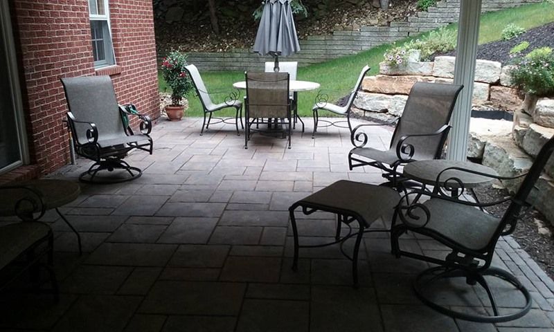Patio with outdoor furniture: chairs, table, and an umbrella, on a stone patio, with a brick building.