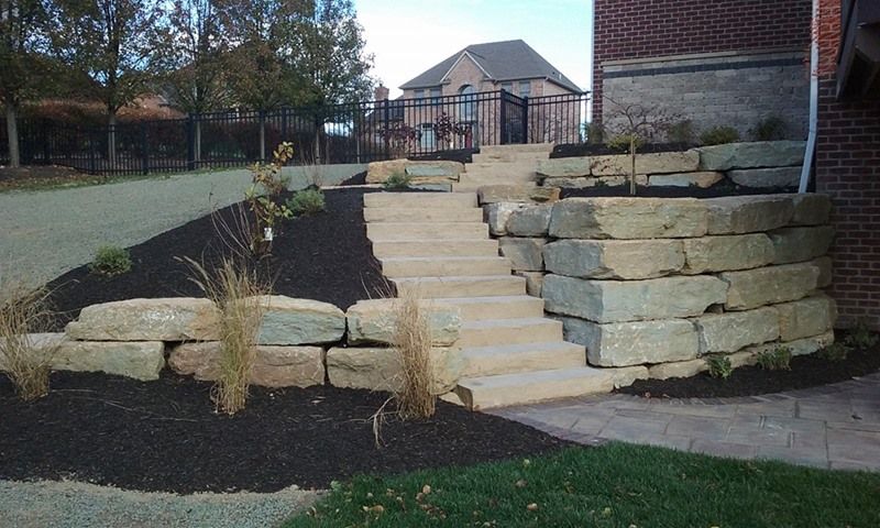 Stone steps and retaining walls with black mulch and grass in front of a house.