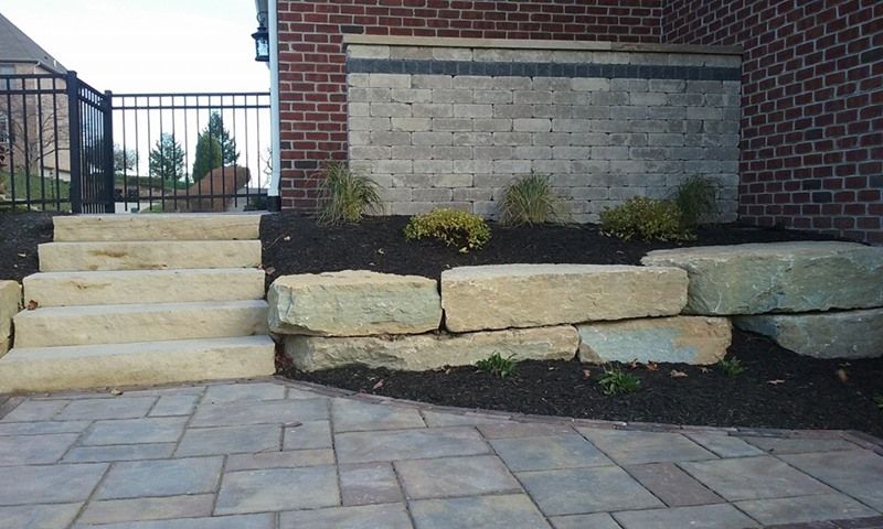 Stone steps and retaining wall leading to a brick building with a decorative water feature.