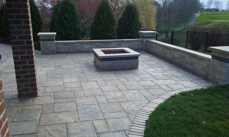 Patio with stone pavers, fire pit, retaining wall, and green lawn.