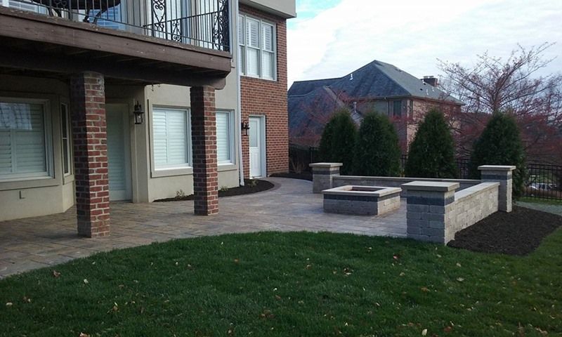 Patio with fire pit and lawn next to a two-story brick and beige house.