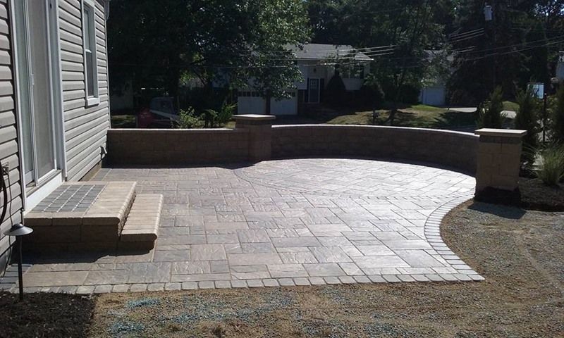 Brick patio with low wall and steps next to a house, sunny day.
