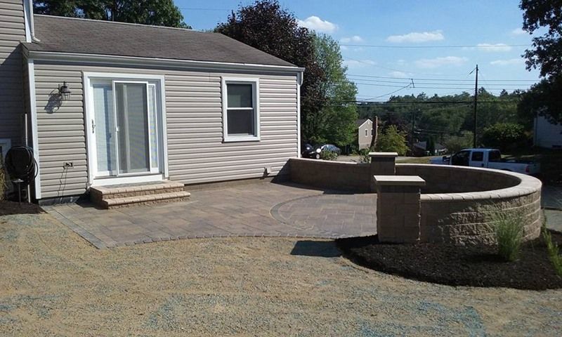 Paved patio with curved retaining wall and house in the background on a sunny day.