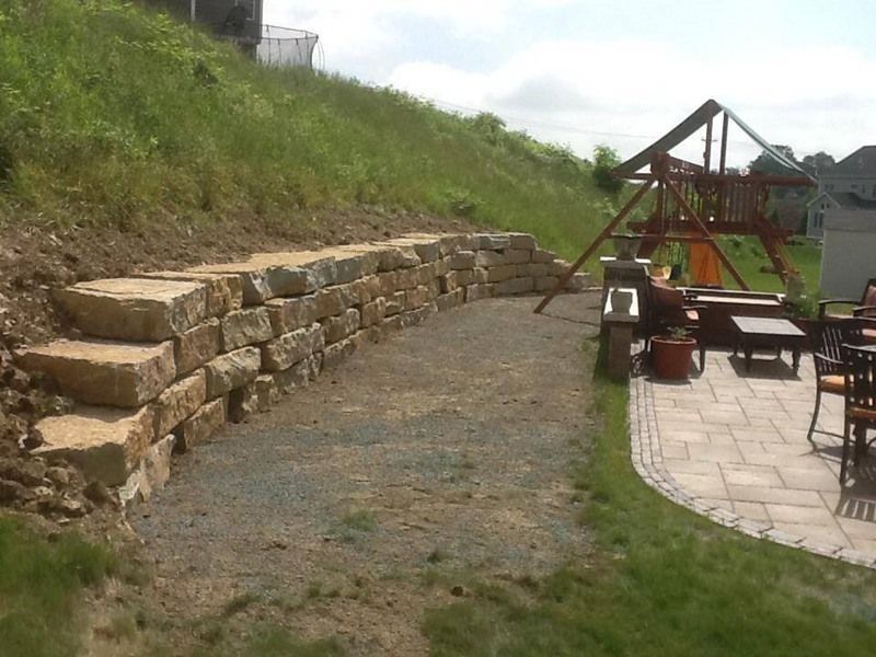 Stone retaining wall on a hillside with gravel pathway, patio, and playground.