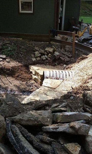 Construction site with a corrugated pipe surrounded by dirt and rocks near a building.