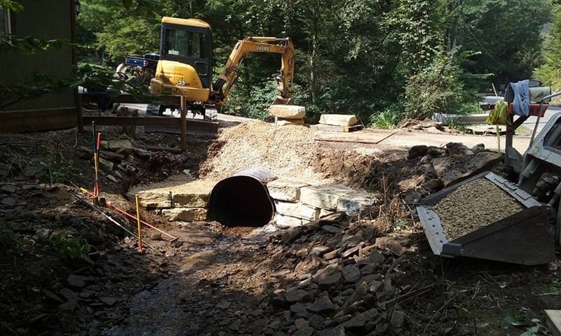 Construction site with excavator and culvert. Dirt, rocks, yellow machinery.