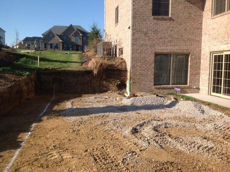 Construction site with a brick house and dirt groundwork. A grassy hill is in the background.