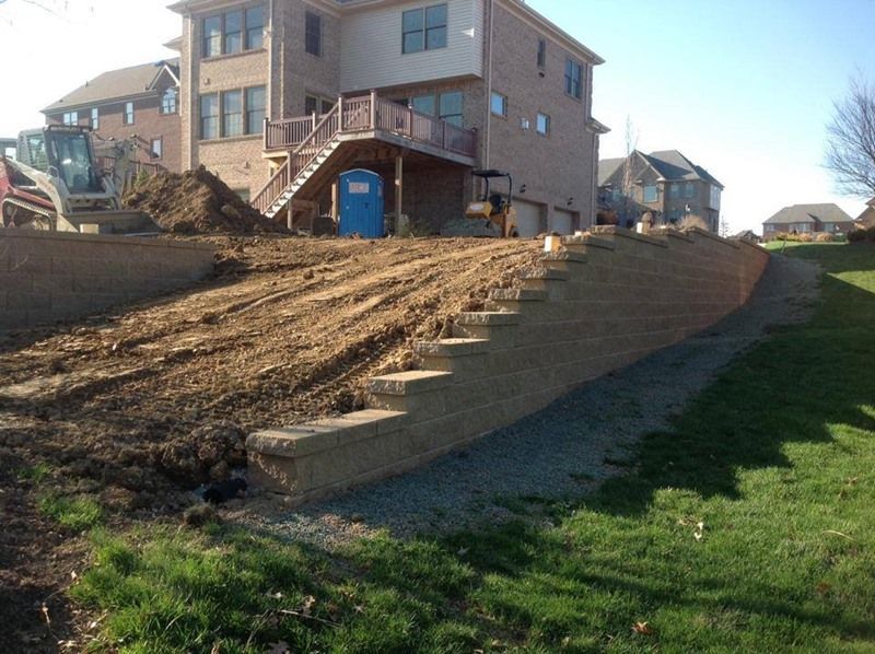 Hillside construction with retaining walls, steps, and a house in the background. A bulldozer is also present.