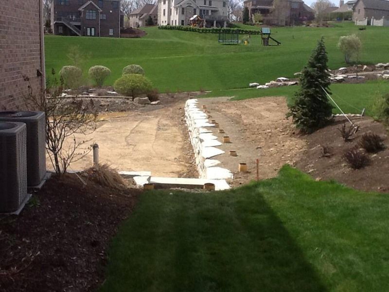 Backyard under construction with graded dirt path, retaining wall, and green grass.