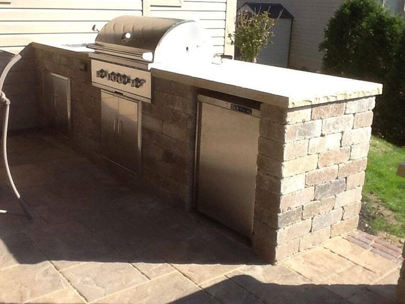 Outdoor brick grilling station with a grill, refrigerator, and countertop.
