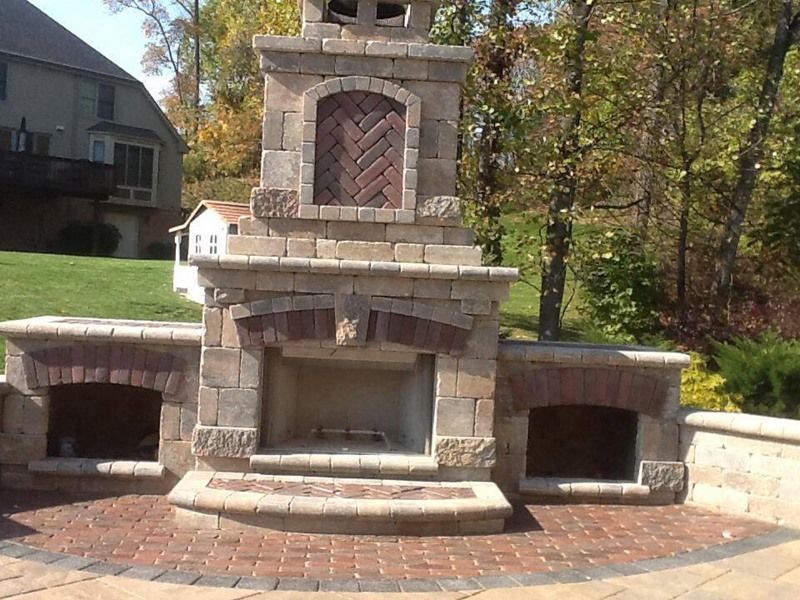 Stone outdoor fireplace with brick accents and side storage, on a brick patio.