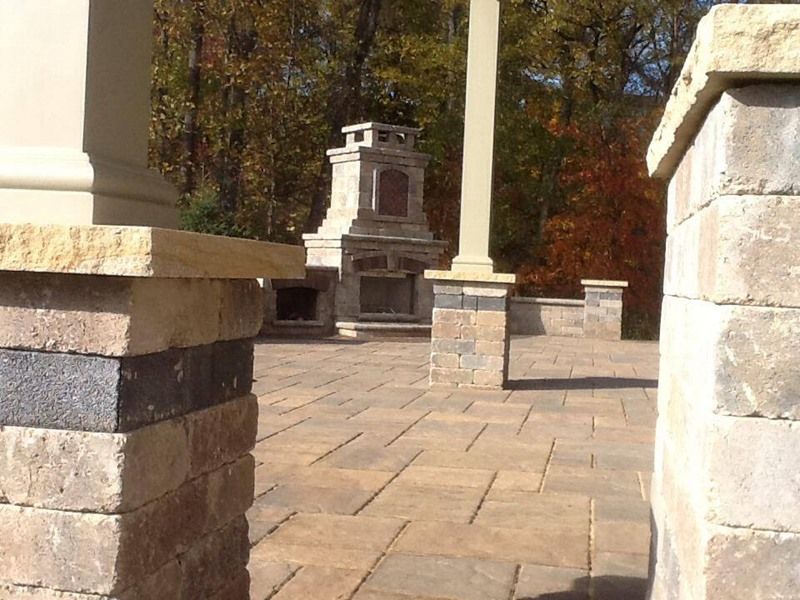 Brick patio with fireplace, columns, and fall foliage in background.