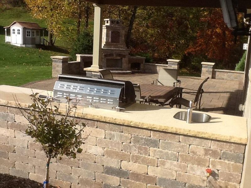 Outdoor patio with brick wall, grill, fireplace, and lounge chairs.