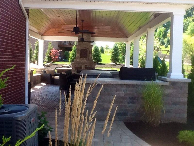 Covered outdoor patio with a fireplace and built-in grill, brick and stone construction.