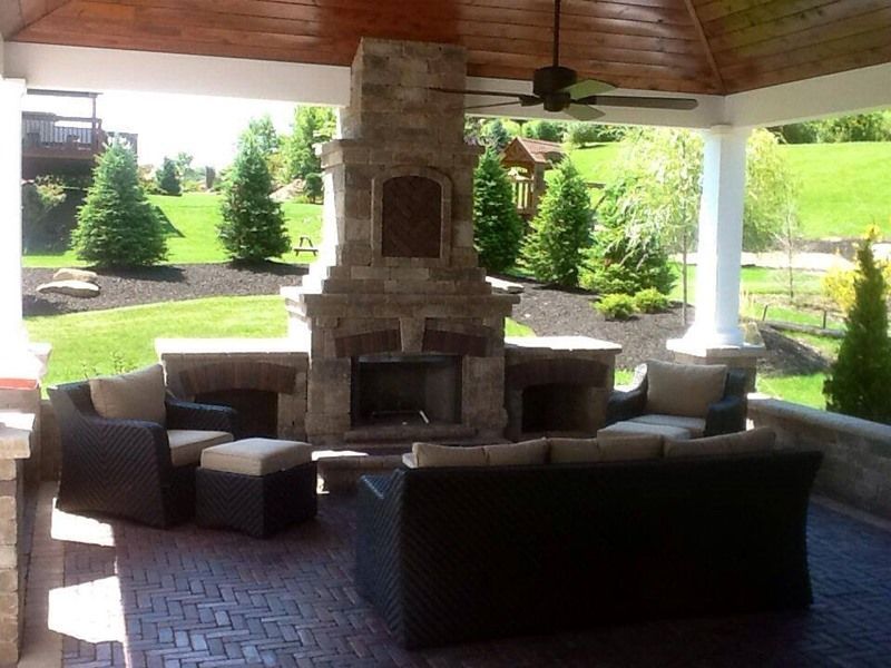 Outdoor patio with stone fireplace, seating area, and lush green lawn in background.