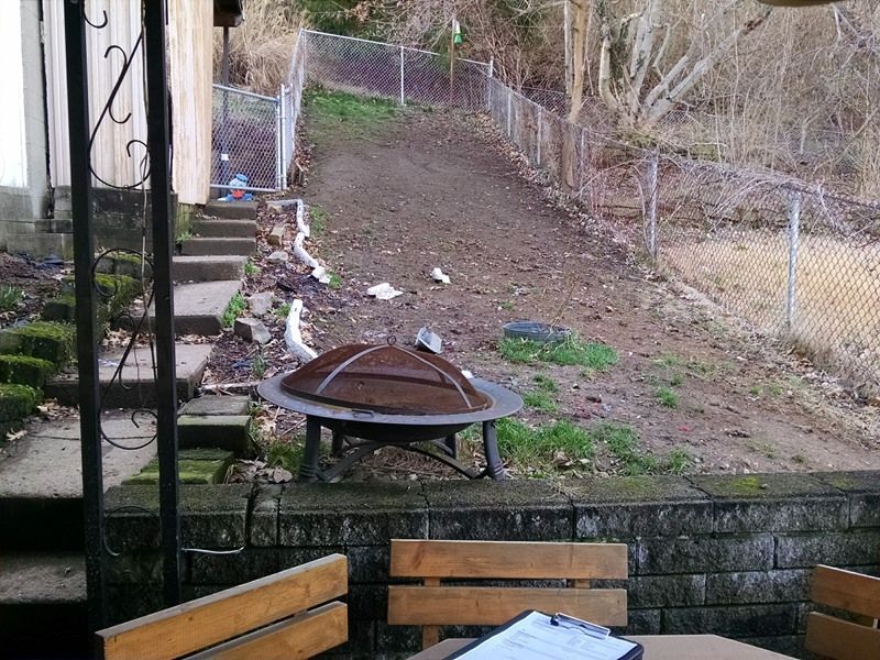 A backyard scene with a fire pit, stairs, and a chain-link fence on a sloped, dirt area.