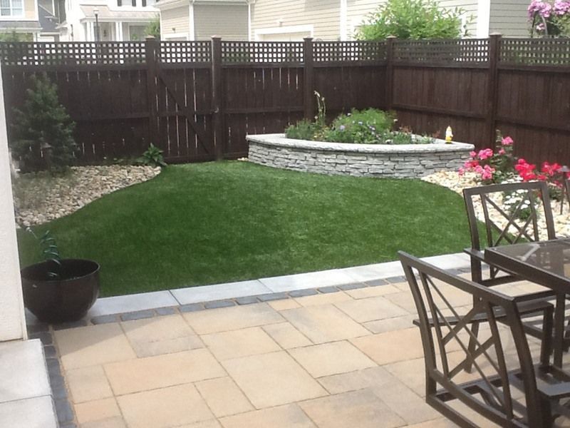 Backyard with patio, lawn, stone-lined garden bed, dark brown fence, and outdoor furniture.