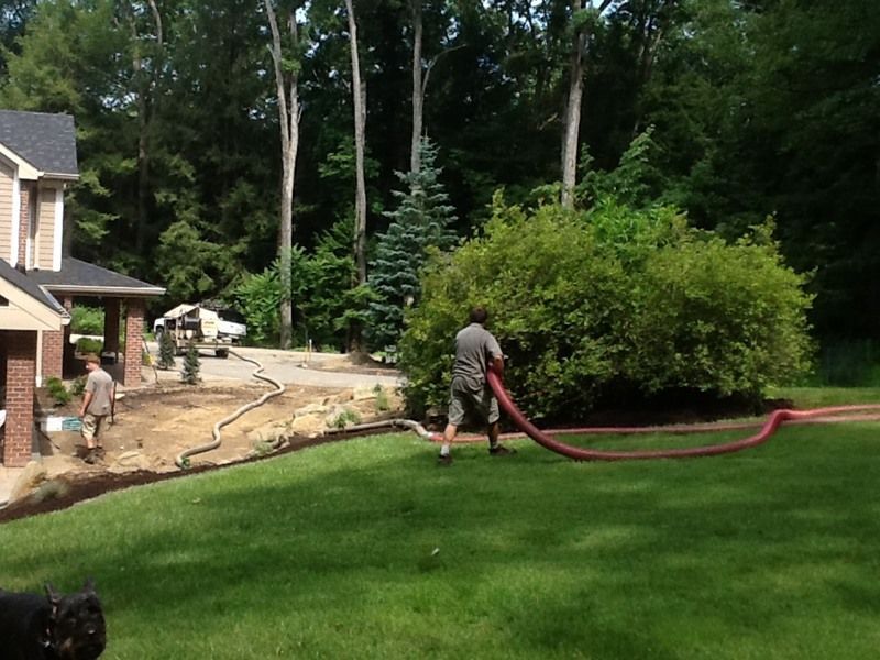 Men spreading mulch with hose, beside a house with a lawn and trees.