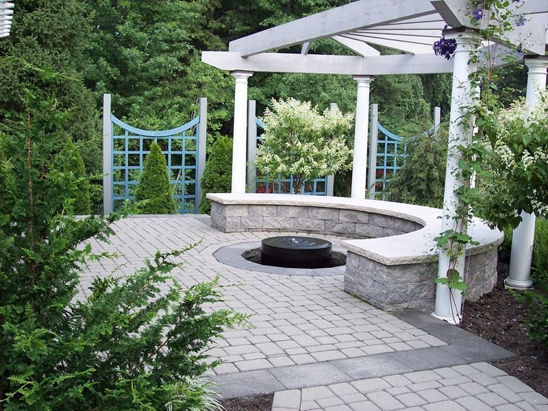 Patio with curved stone bench around a fountain, surrounded by a pergola and blue lattice.