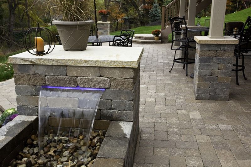 Water feature with a stacked stone wall, a small waterfall, and patio pavers.