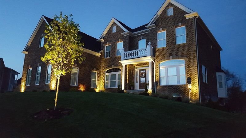 Two-story brick house illuminated at night, with landscaping and spotlights on the facade.