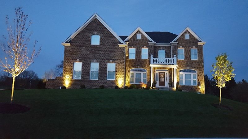 Two-story brick house illuminated at night by ground spotlights; trees on either side.