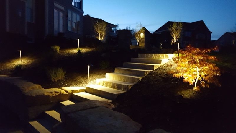 Illuminated stone steps leading up a hillside at night. Pathway lights and landscaping lights highlight the way.