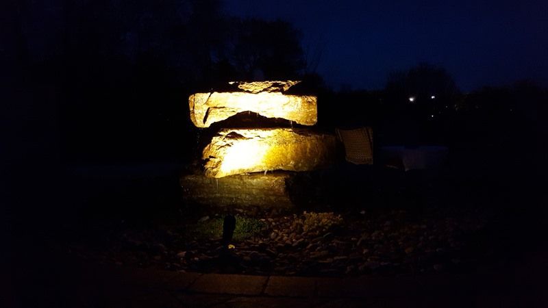 Stacked stone fountain illuminated by warm light at night.