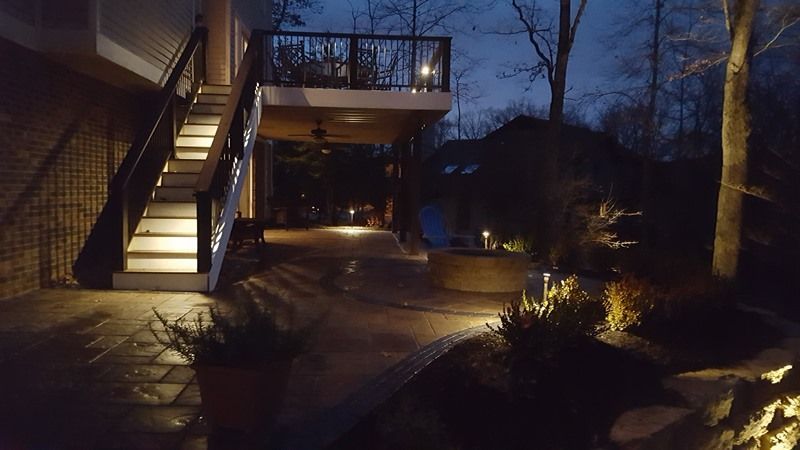 Night view of a deck and stairs illuminated with lights, leading to a yard with landscaping.