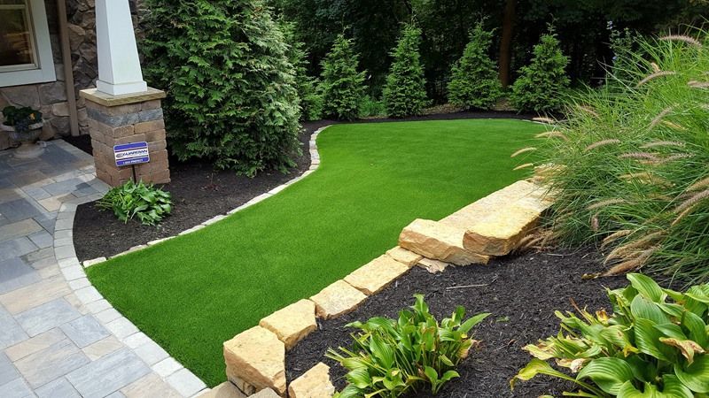 Manicured front yard with green lawn, stone edging, black mulch, and various plants.