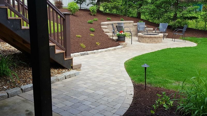Stone pathway leads to a backyard patio with fire pit, seating, and landscaping with mulch.