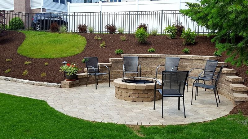 Stone patio with fire pit, seating, and terraced landscaping with grass and mulch.