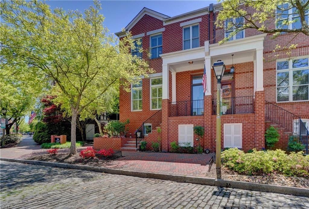 A large brick house with a cobblestone driveway and trees in front of it.