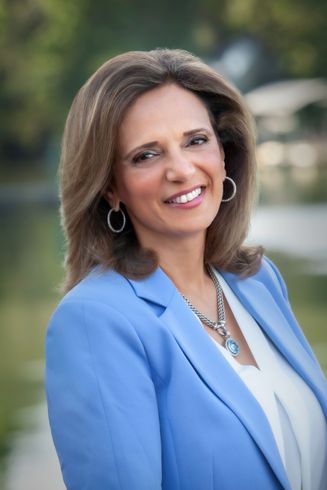 A woman in a blue jacket and white shirt is smiling for the camera.