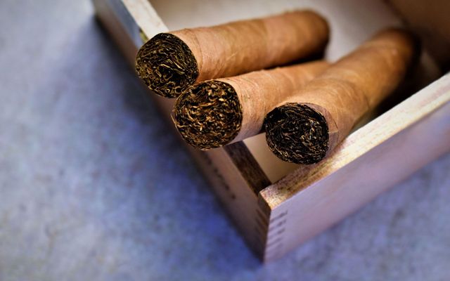Three cigars are in a wooden box on a table.