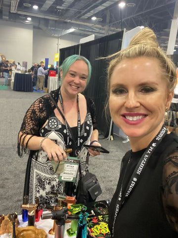 Two women are posing for a picture at a convention.